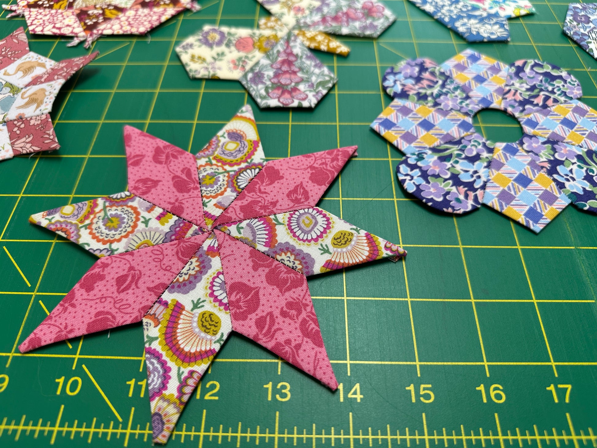 Colorful star-shaped fabric pieces on a green cutting mat with grid lines.