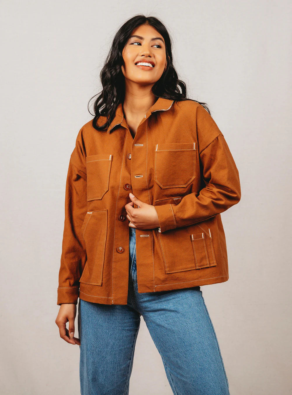 Woman wearing a brown jacket and blue jeans against a plain background