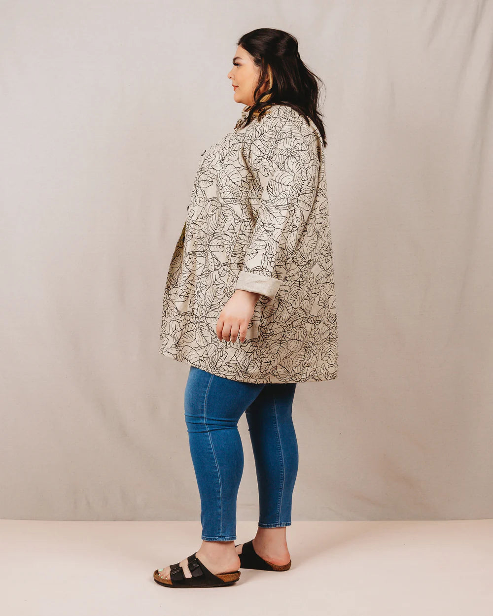 Woman wearing a patterned coat and blue jeans against a plain background