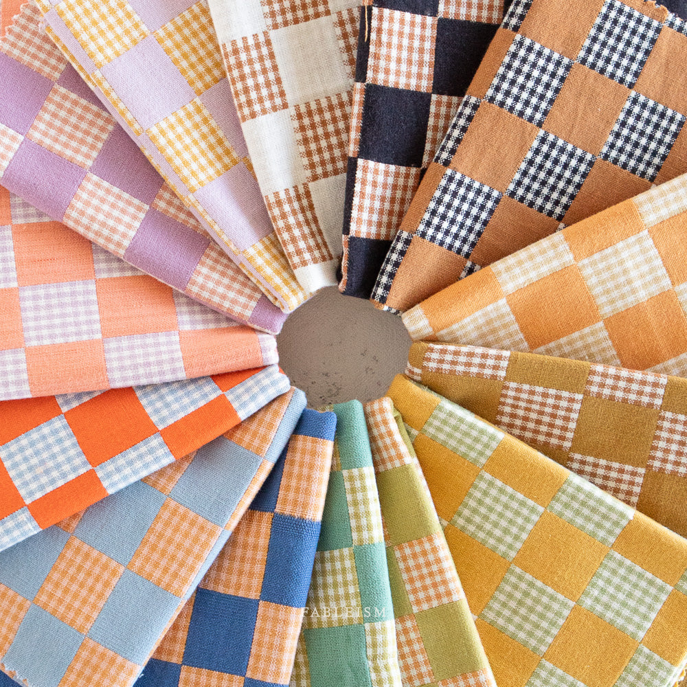 Collection of checkered fabric from the Fableism Checkmate Checkers line in various colors arranged in a circular pattern.