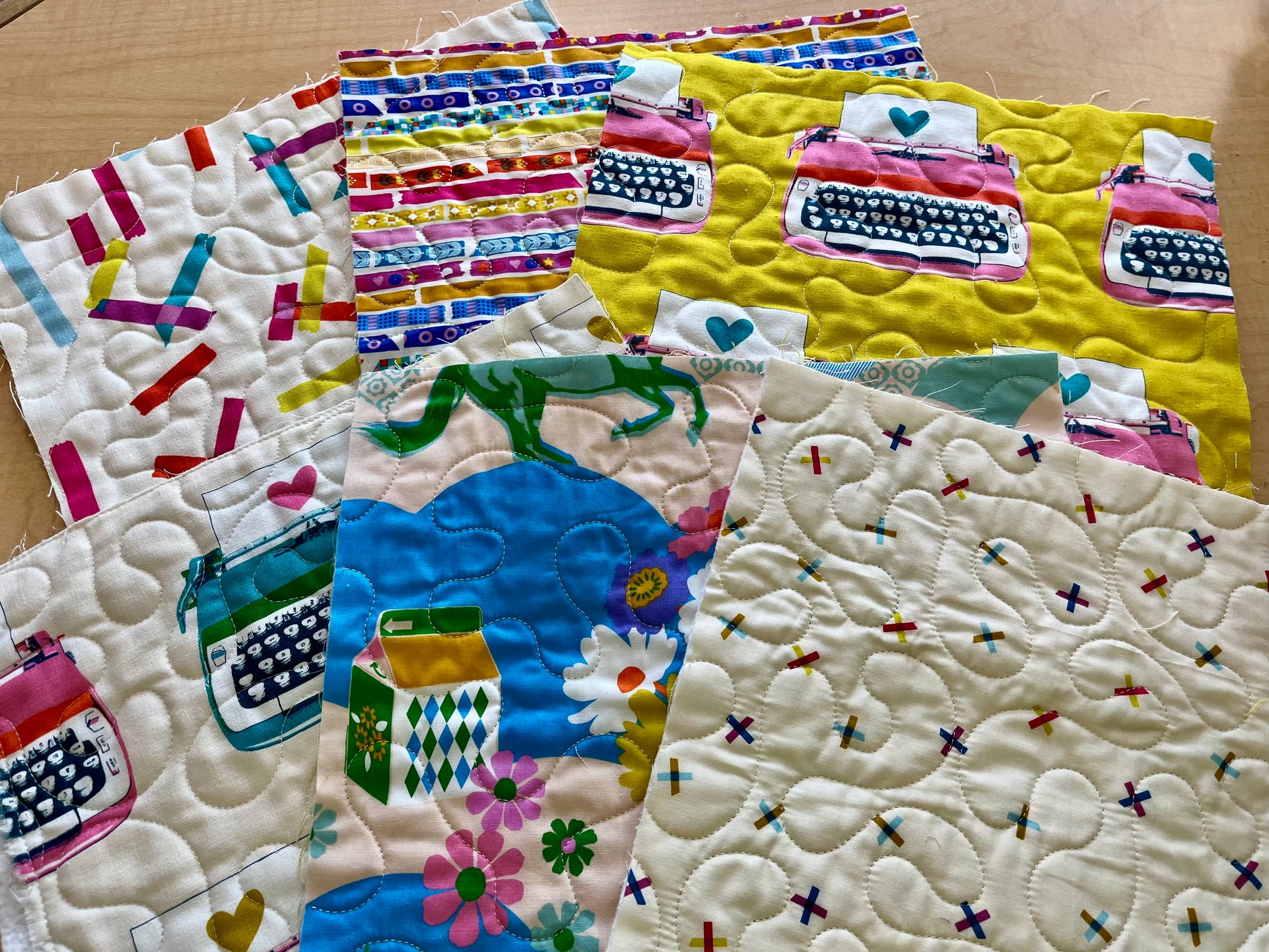 Collection of colorful quilted fabric panels with various patterns on a wooden surface.