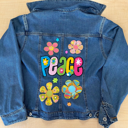 Blue denim jacket with colorful flowers and 'PEACE' text on a beige background