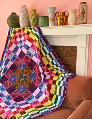 Colorful quilt draped over a sofa with decorative vases on a mantelpiece.