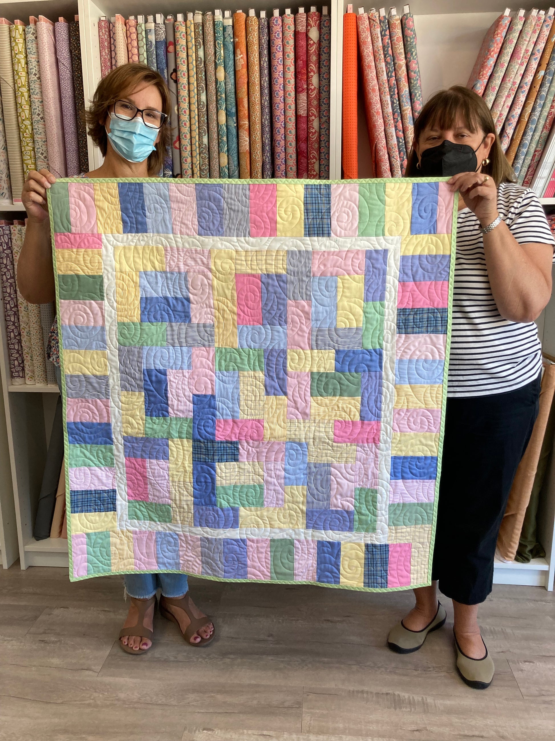 Person holding a colorful quilt next to fabric rolls