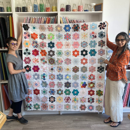 Darcy and Lana hold up a quilt top filled with EPP hexagon flowers