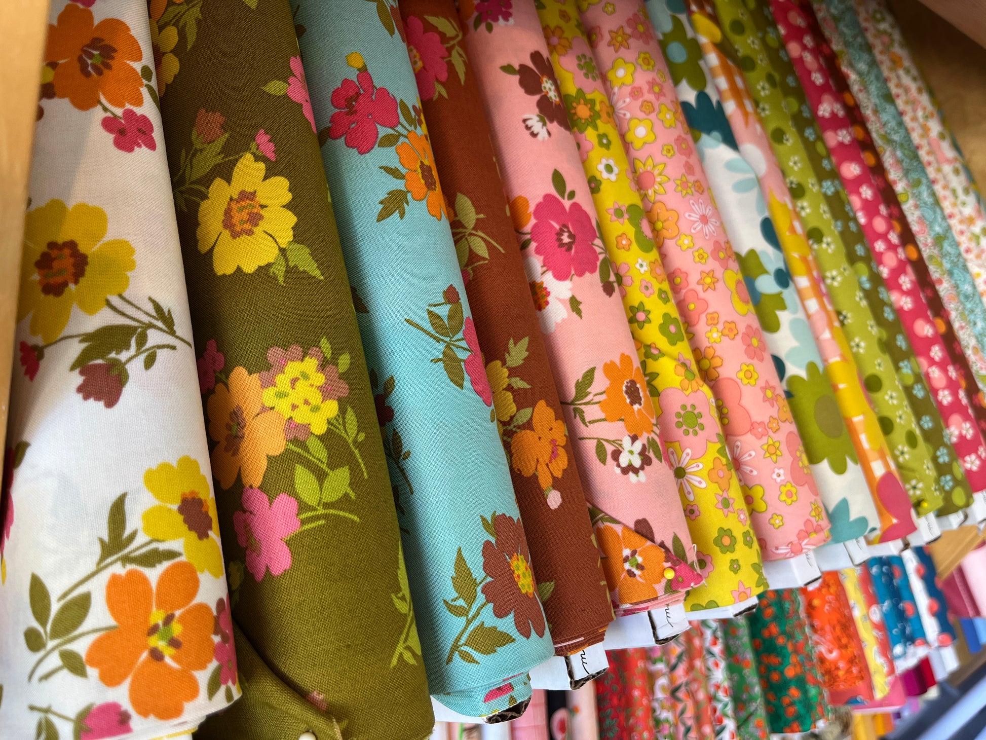 Row of colorful floral fabric rolls on a wooden surface