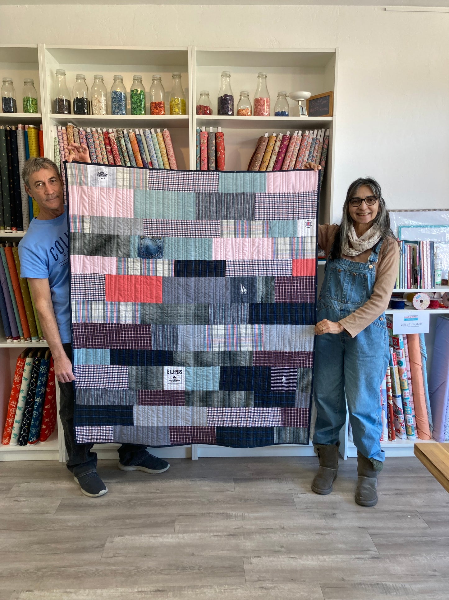 Two people holding a patchwork quilt in a fabric store.