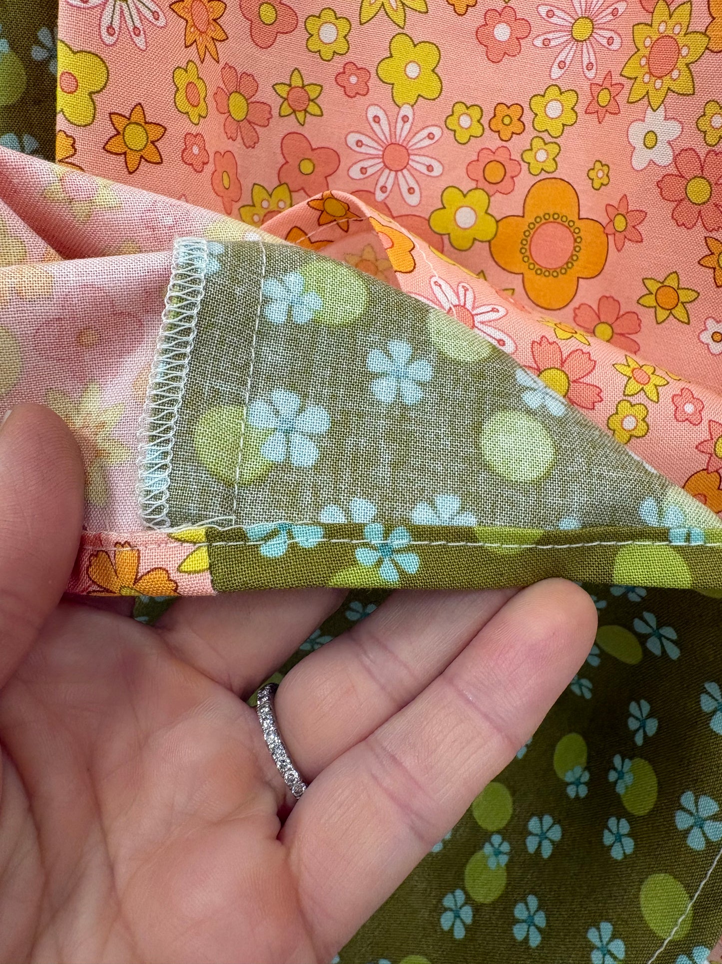 Close-up of hands holding fabric with floral patterns shoing a hem.