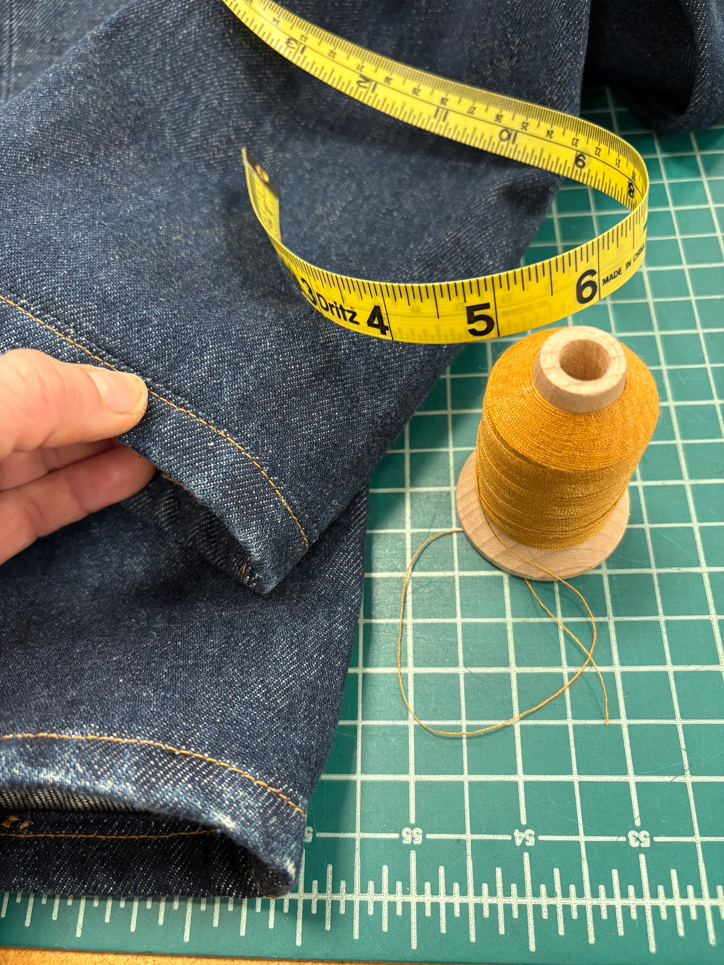 Measuring denim fabric with a tape measure and spool of thread on a grid background