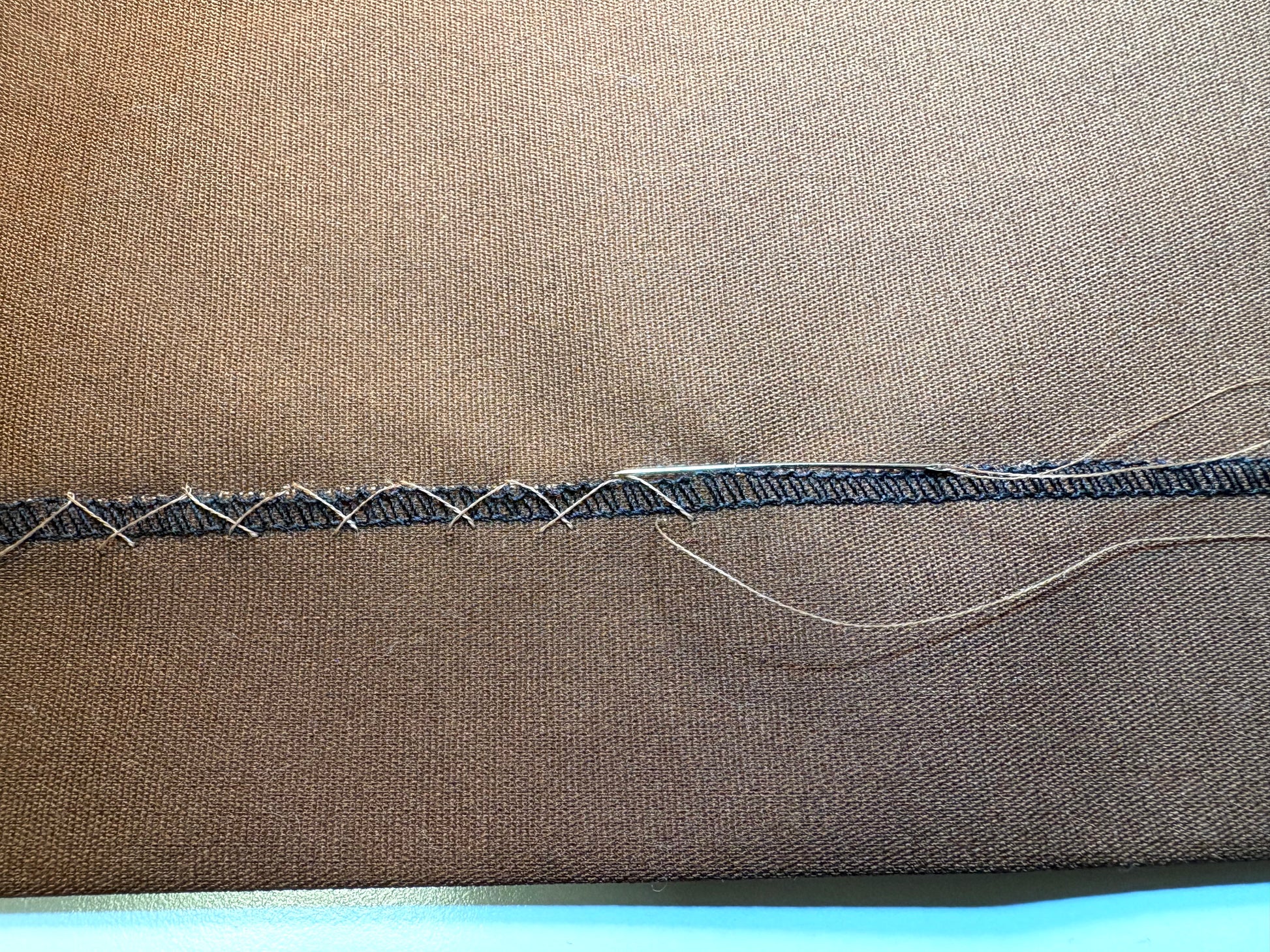 Close-up of a brown fabric with visible hem stitches on a blue background