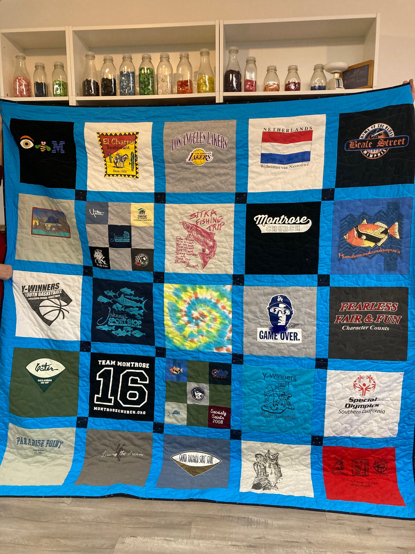 Quilt made from various t-shirts with different designs and text, displayed on a wooden floor.