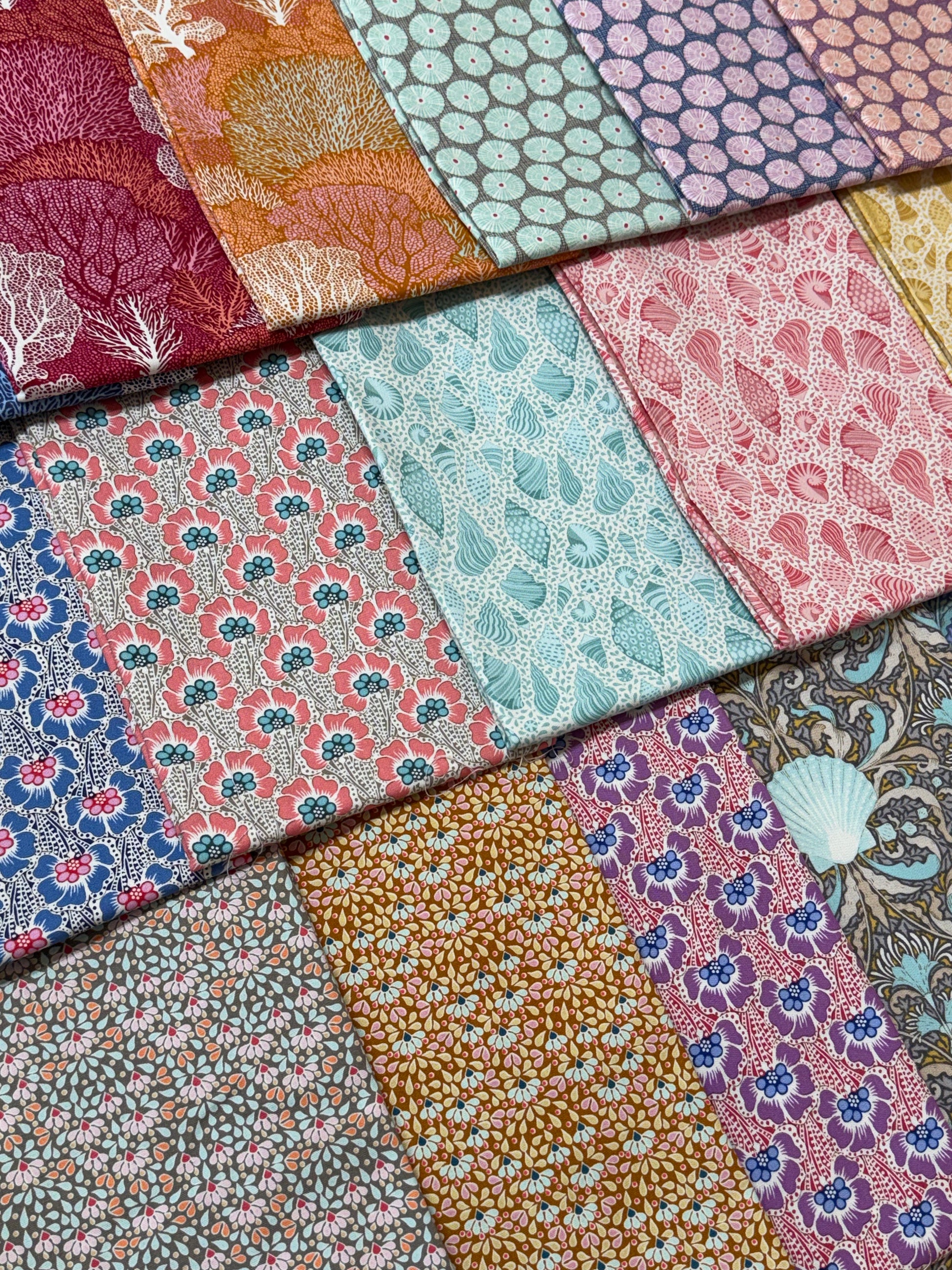 A close-up arrangement of multiple patterned fabric swatches in assorted colors and designs, including floral, paisley, and coral motifs.