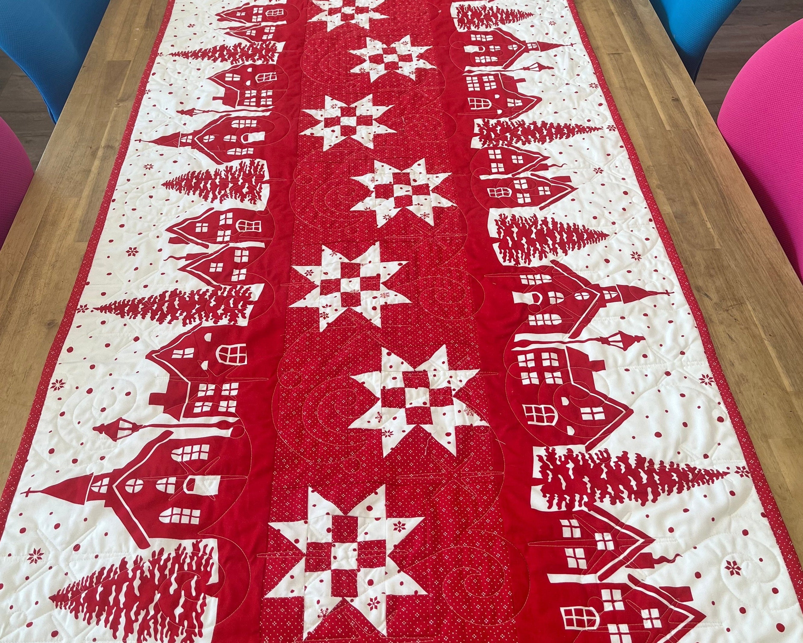 Red table runner with white snowflake and village design on a wooden table.