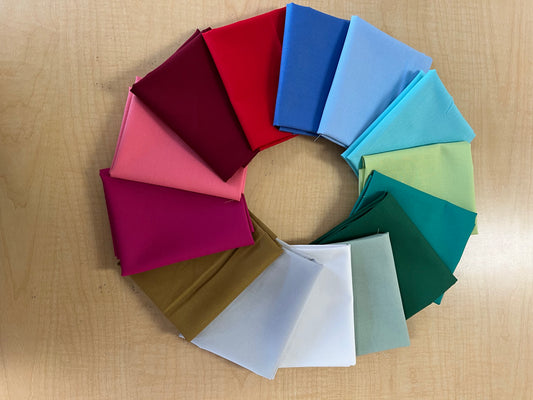 Fabric swatches in various colors arranged in a circular pattern on a wooden surface.