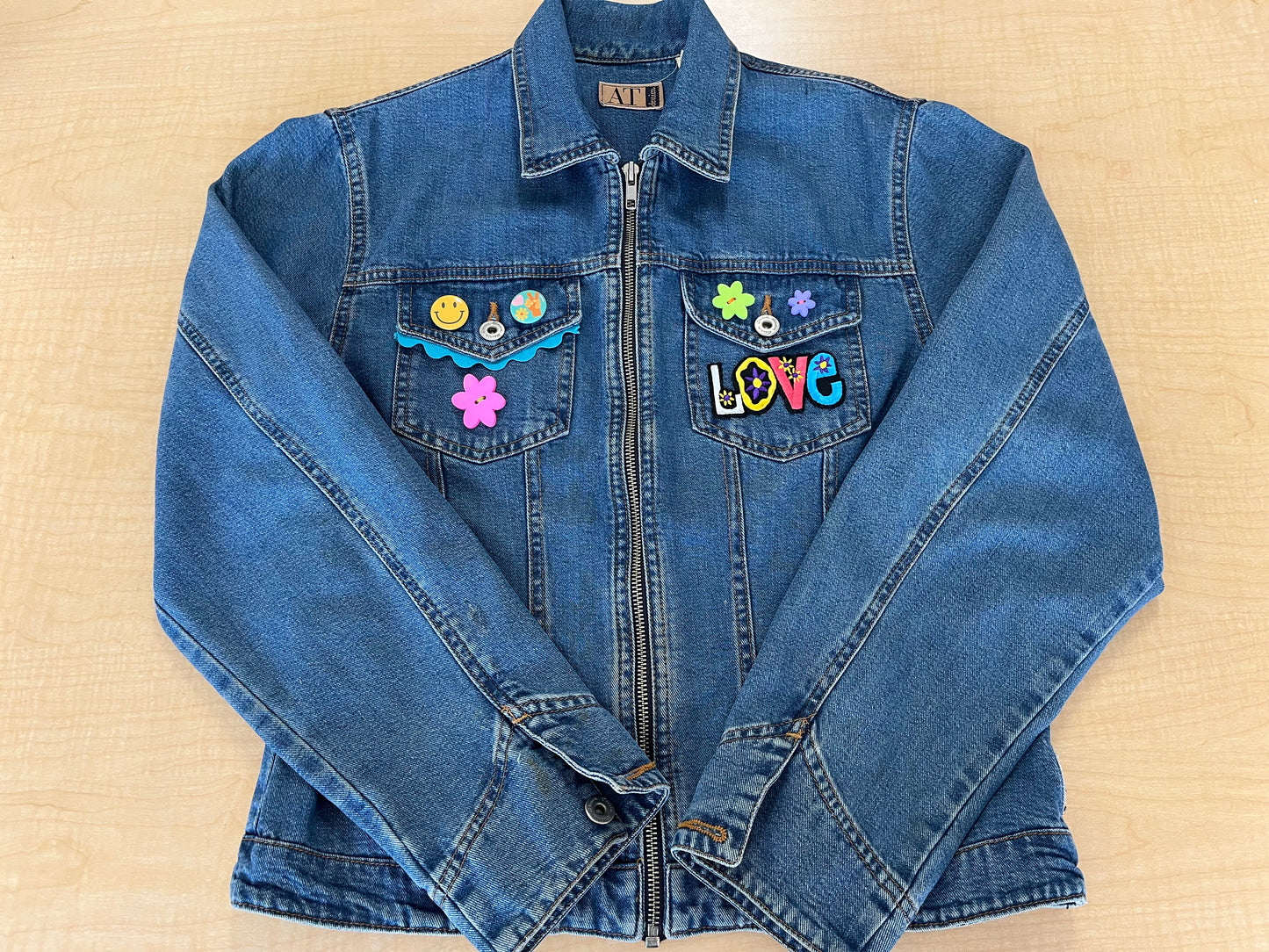 Blue denim jacket with colorful patches on a beige surface