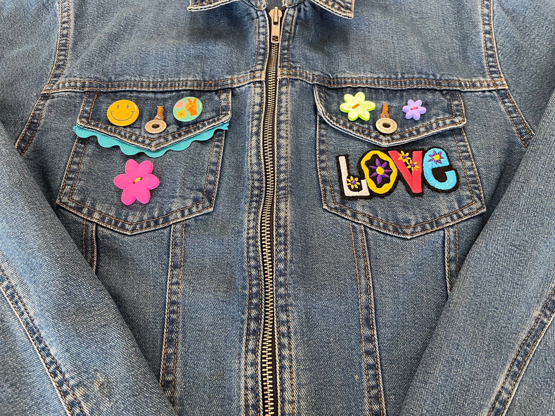 Denim jacket with colorful patches including flowers and the word 'LOVE'.