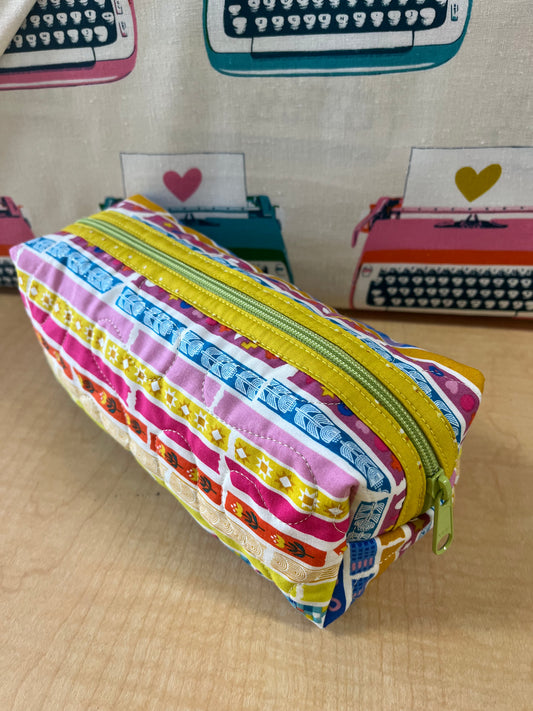 Colorful striped pencil case on a wooden surface with typewriter-themed decorations in the background.