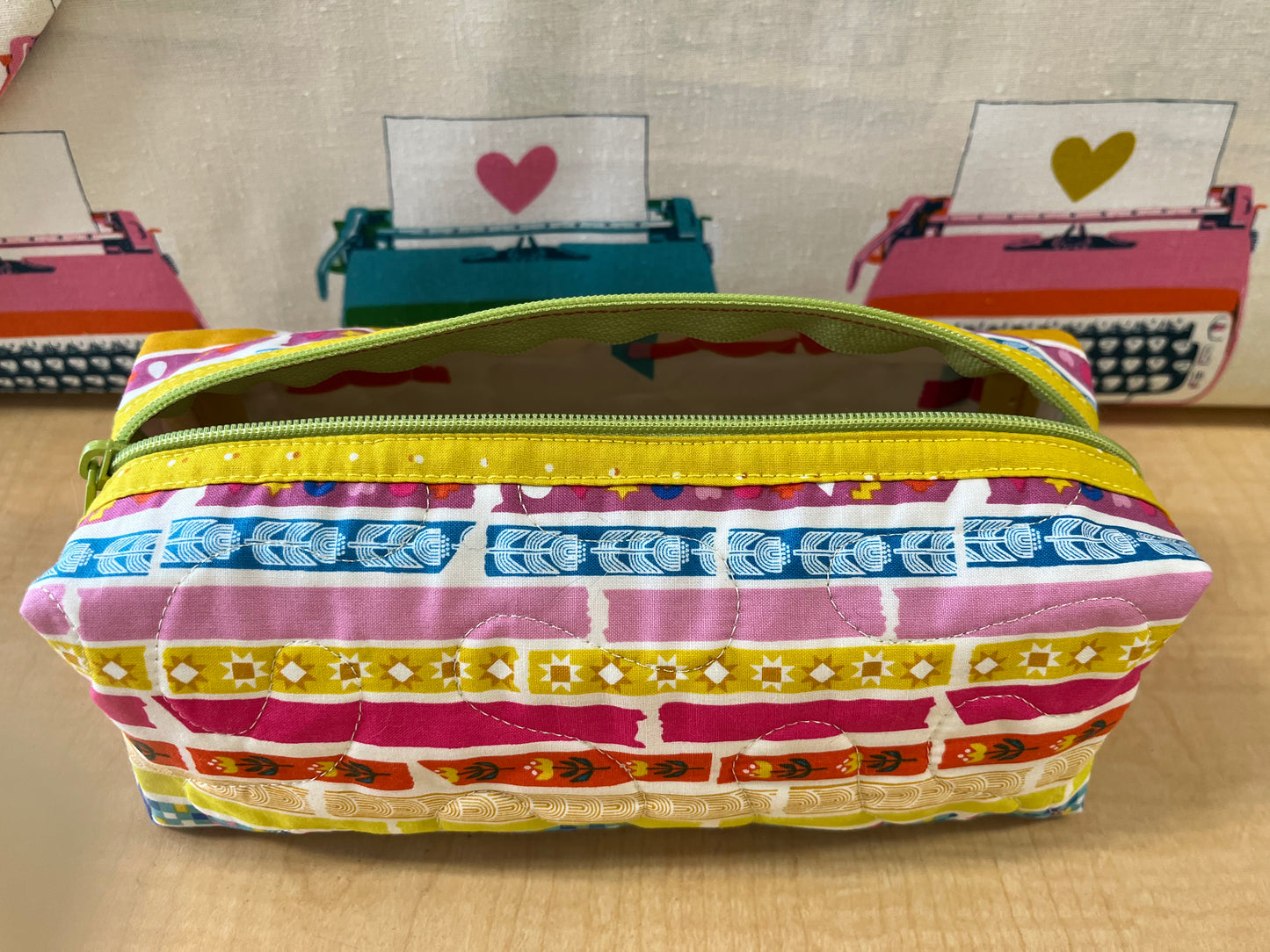 Colorful striped pencil case with a yellow zipper on a wooden surface.