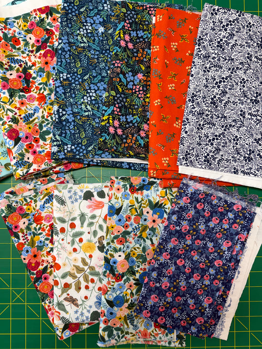 A collection of folded fabric pieces with various floral and botanical patterns in multiple colors, arranged on a green cutting mat.