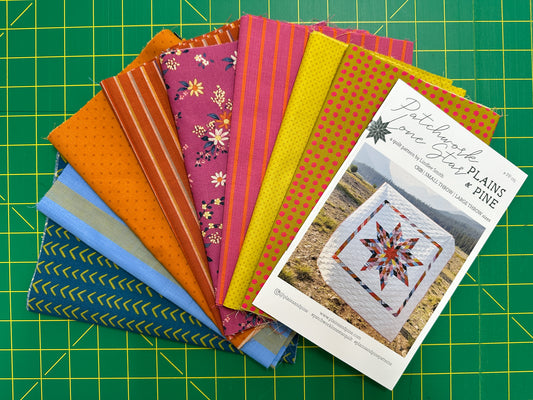 Stack of fabric swatches with a quilt pattern leaflet on a green cutting mat