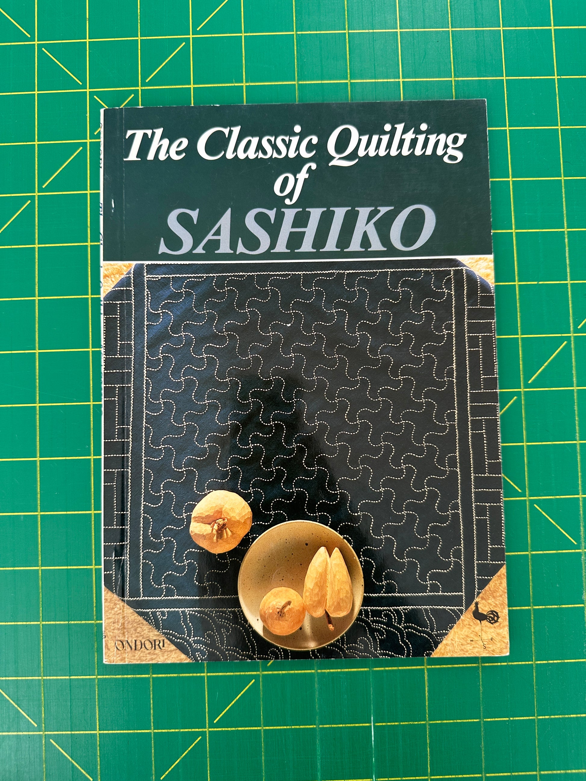 Book titled 'The Classic Quilting of Sashiko' on a green grid background