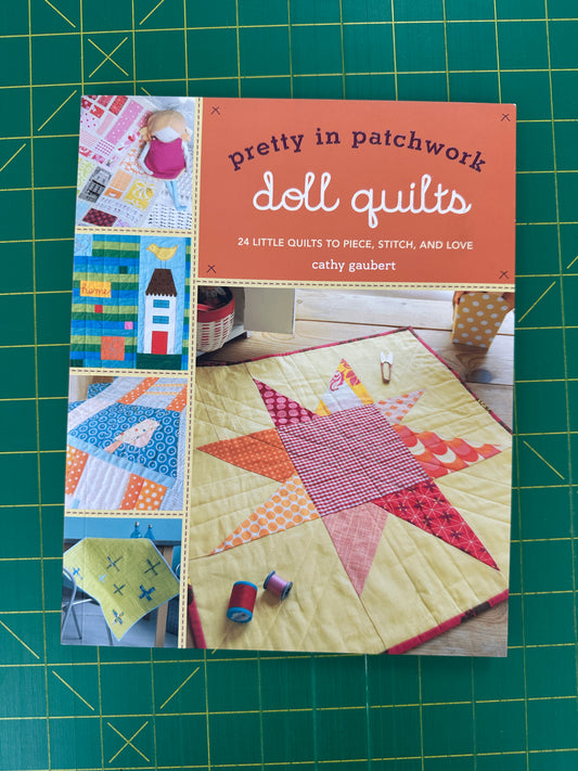 Book titled 'Pretty in Patchwork Doll Quilts' on a green cutting mat
