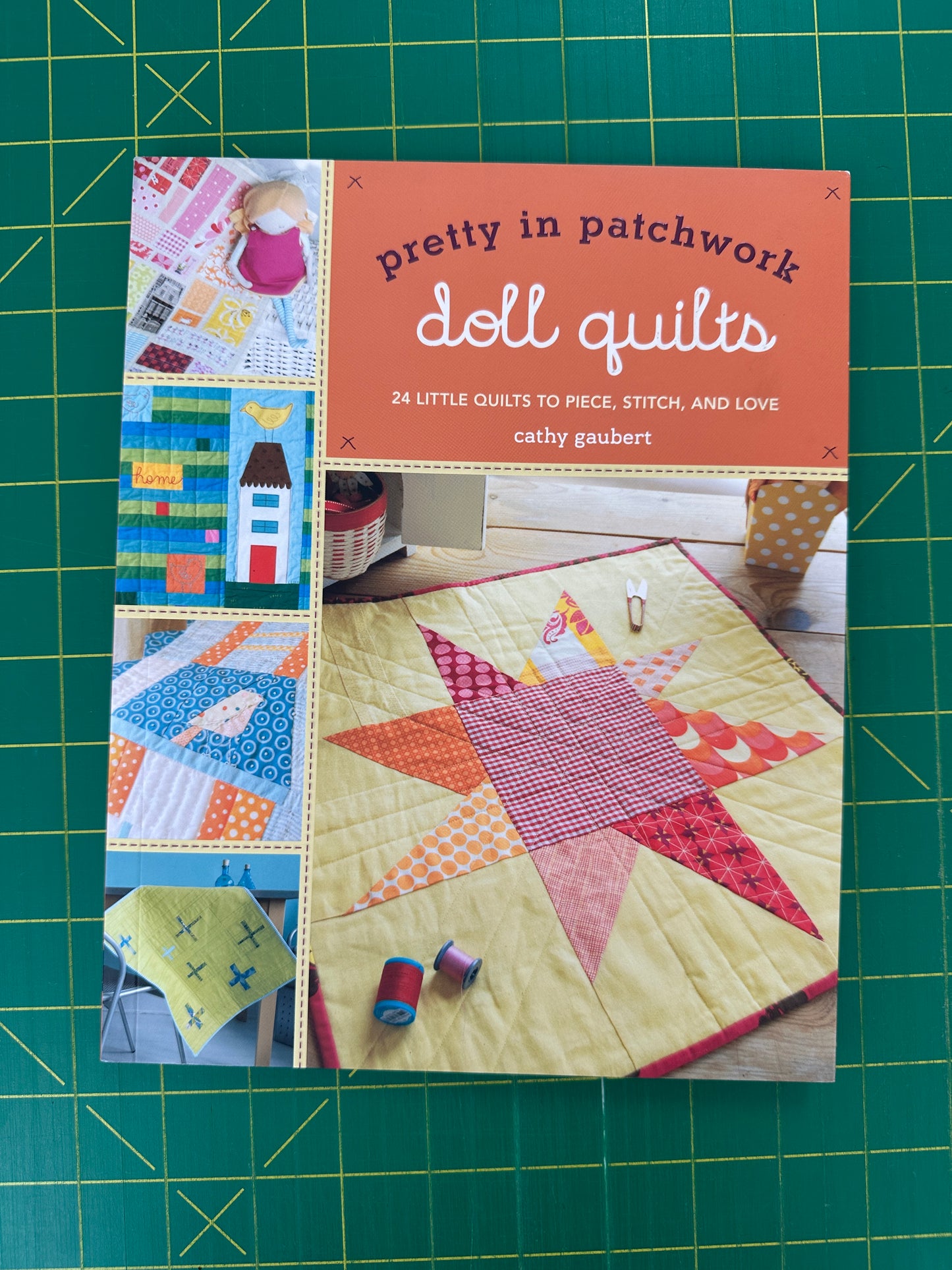 Book titled 'Pretty in Patchwork Doll Quilts' on a green cutting mat