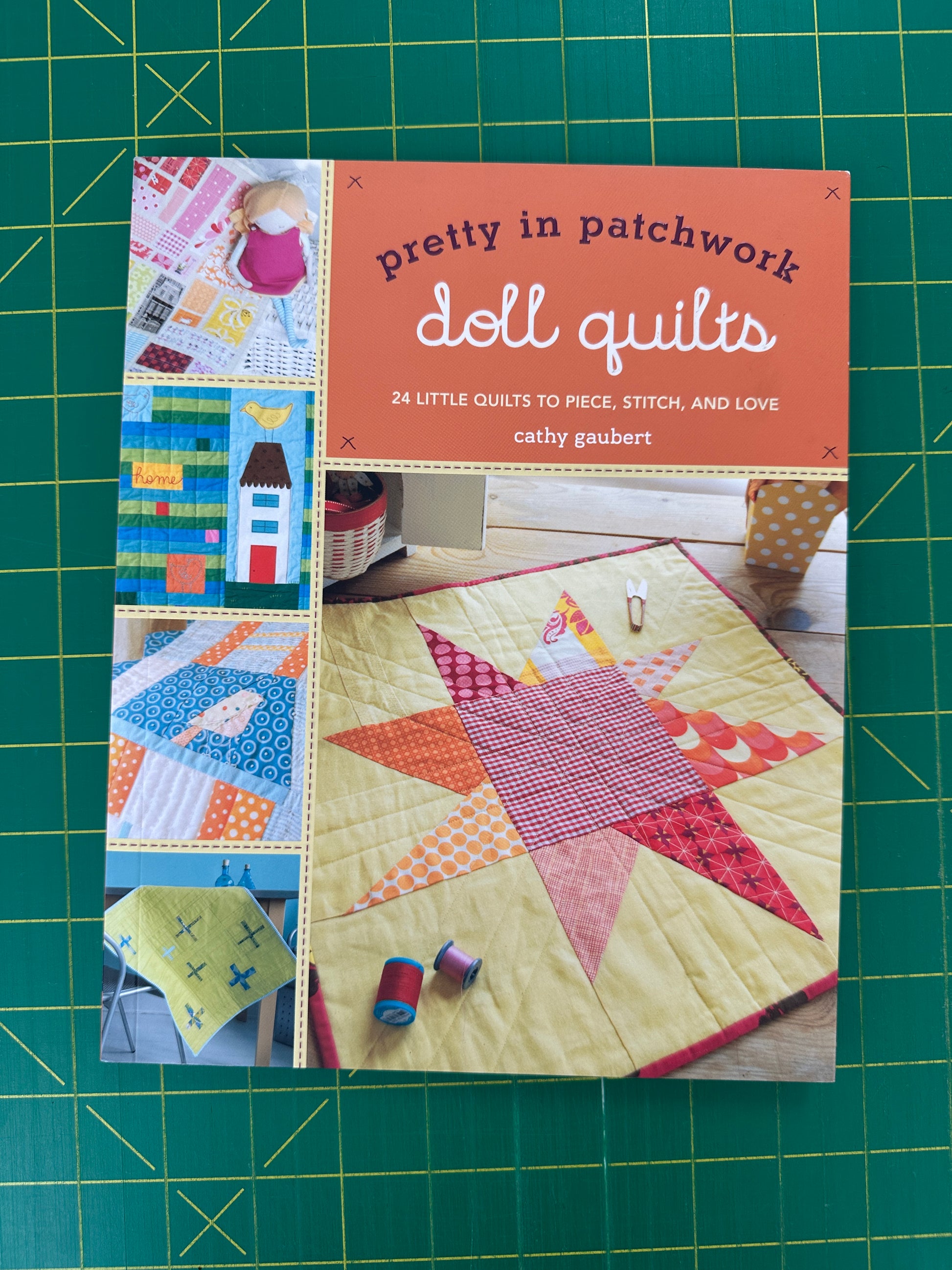 Book titled 'Pretty in Patchwork Doll Quilts' on a green cutting mat