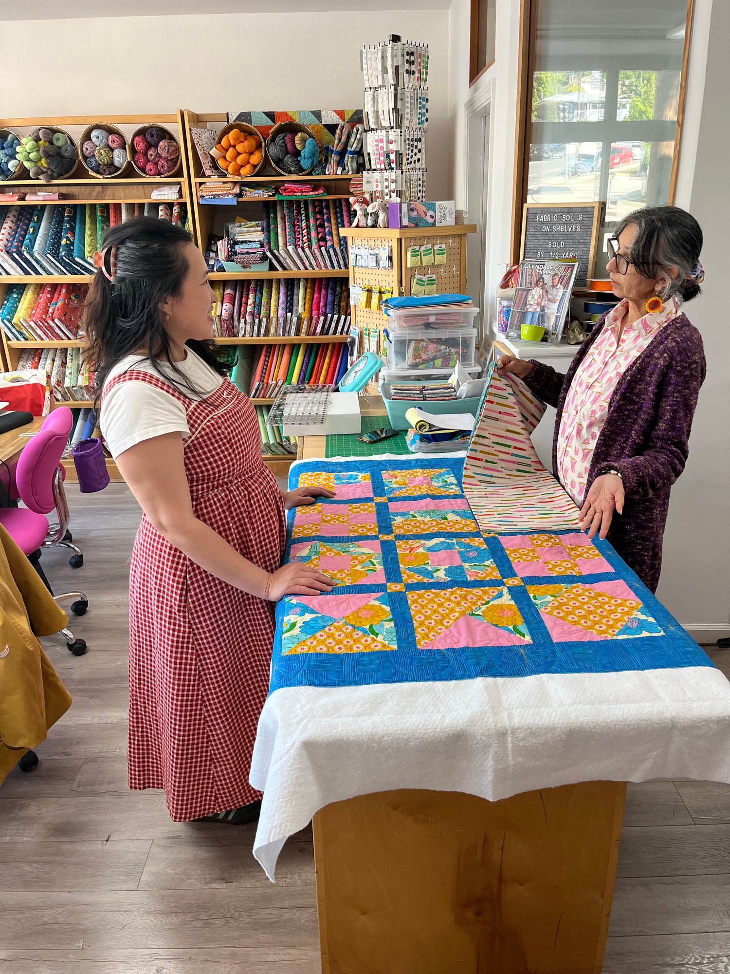 2 people stand on either side of a table with a quilt in between them