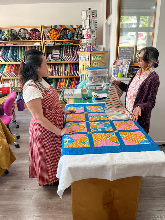 2 people stand on either side of a table with a quilt in between them