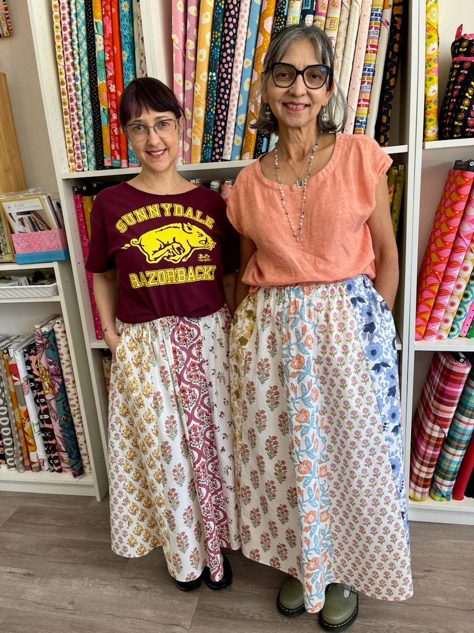 Two women standing in front of a shelf filled with colorful fabric rolls.
