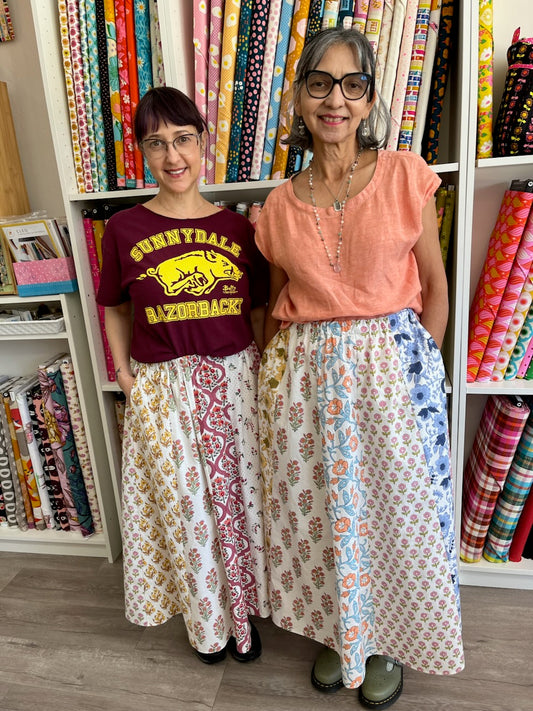 Two women standing in front of a shelf filled with colorful fabric rolls.