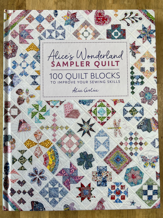 image shows a book titled alice's wonderland sampler quilt. 100 quilt blocks to improve your sewing skills. cover design is mini quilt blocks.