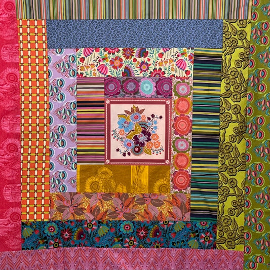 A colorful patchwork quilt or fabric artwork made of multiple patterned fabric panels arranged in concentric squares, including floral, striped, geometric, and paisley designs in pink, blue, green, orange, yellow, and purple.