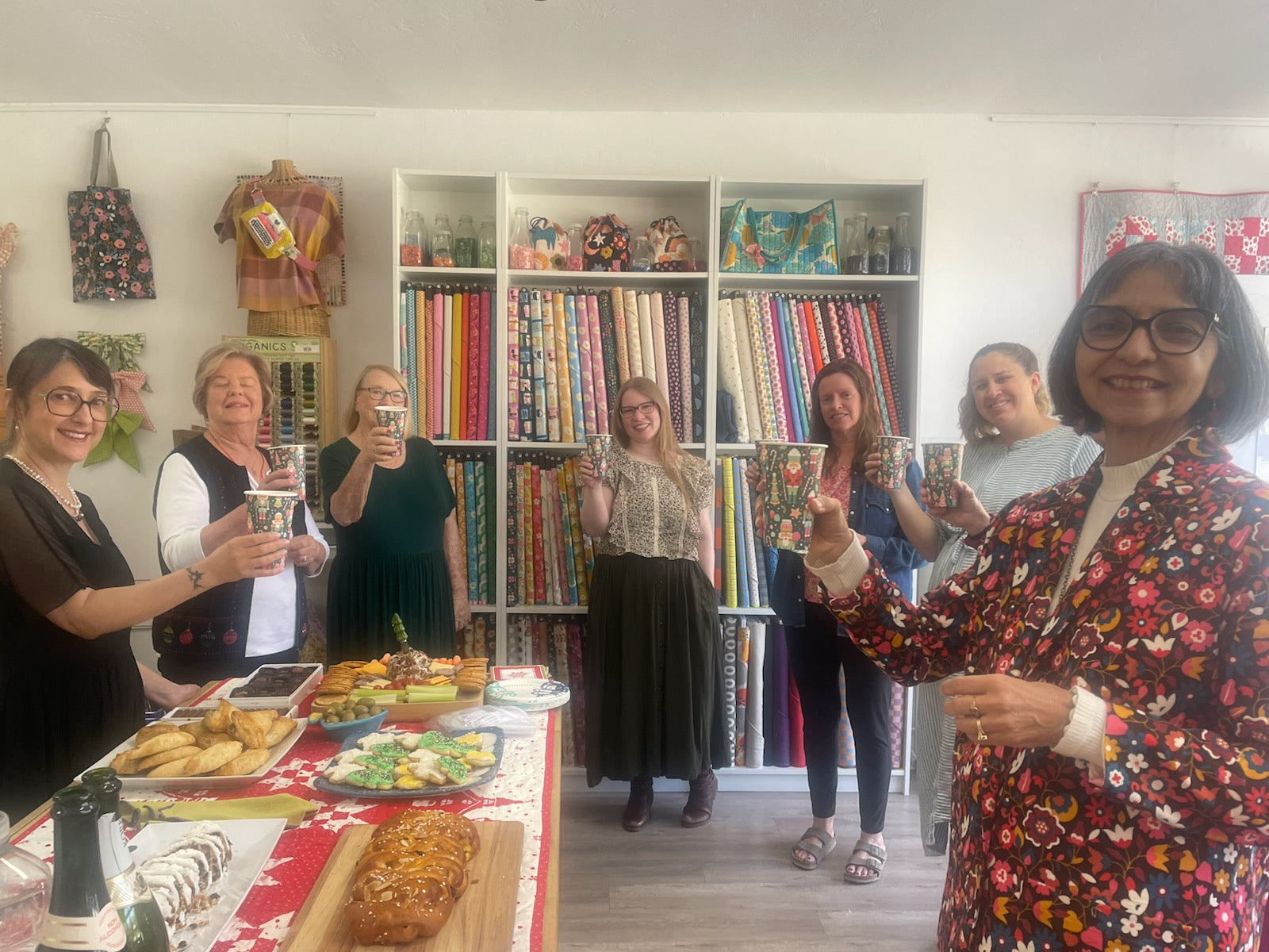 Group of people celebrating with drinks in a room filled with bookshelves and fabric.