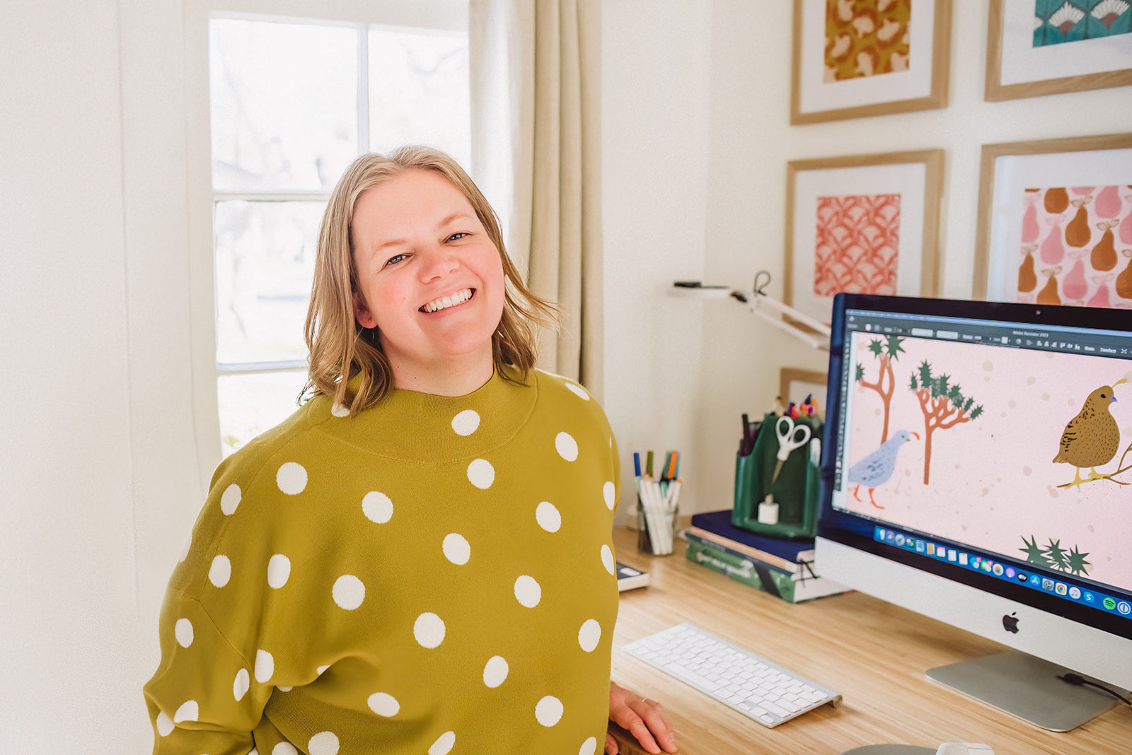 Person in a polka dot shirt standing in front of a computer with artwork on the screen.