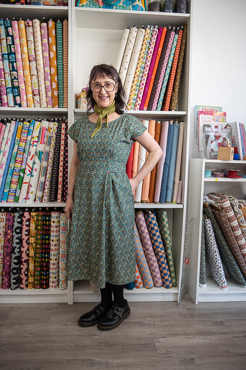 Woman standing in front of a bookshelf filled with colorful fabric rolls.