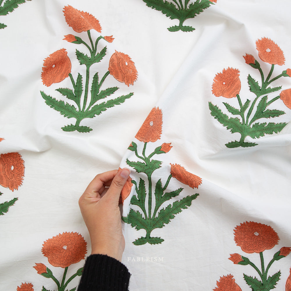 Hand holding fabric with orange floral patterns on a white background