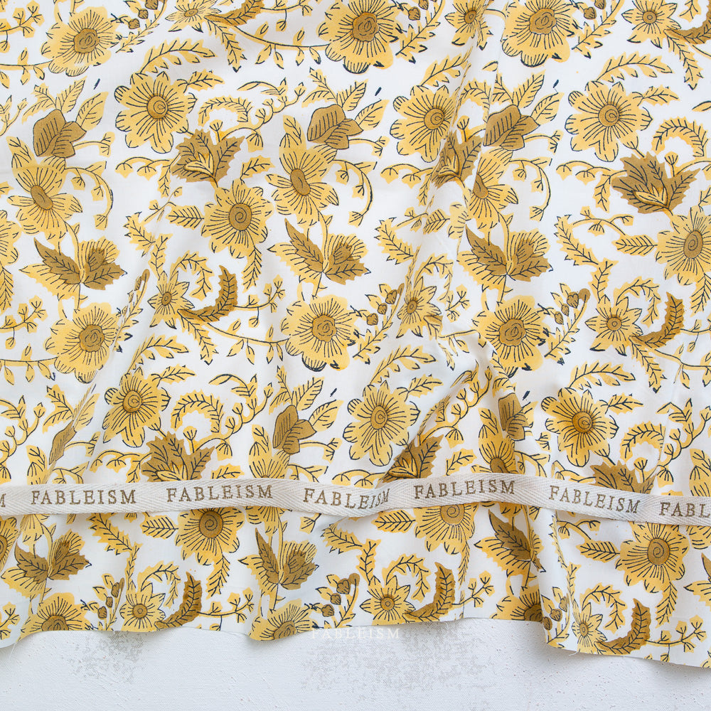 Gold floral pattern on white fabric with 'Fableism' branding.