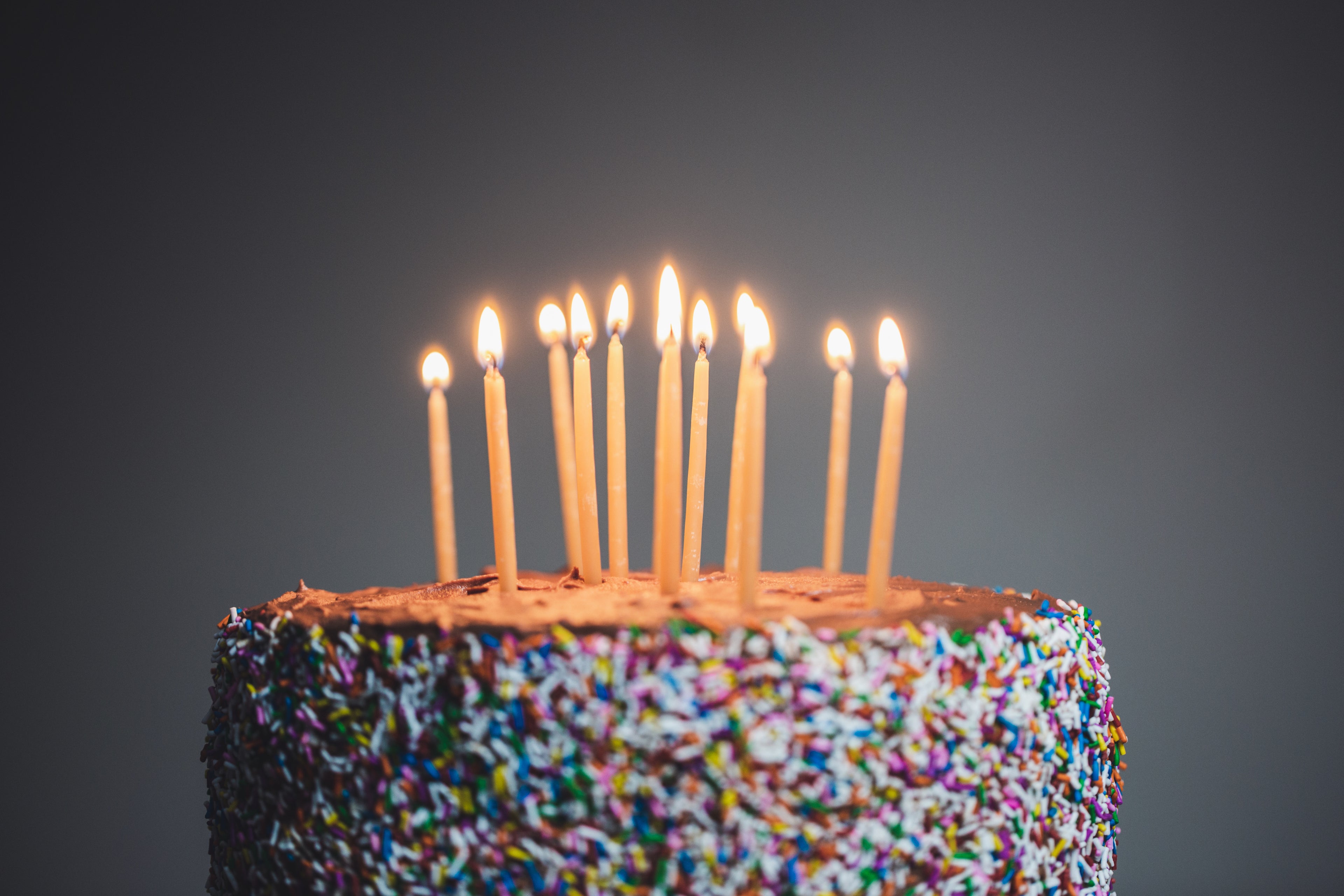 Candles lit on a birthday cake with sprinkles, against a grey background