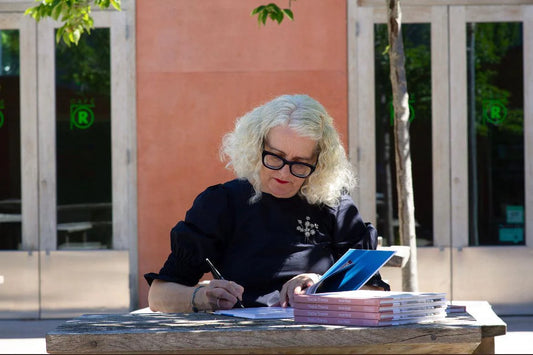 platinum haired woman sits at a table signing books