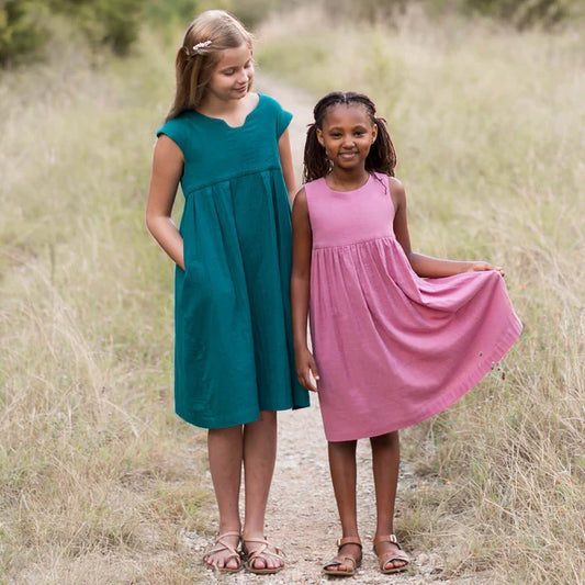 Two young girls in colorful dresses standing in a grassy field.