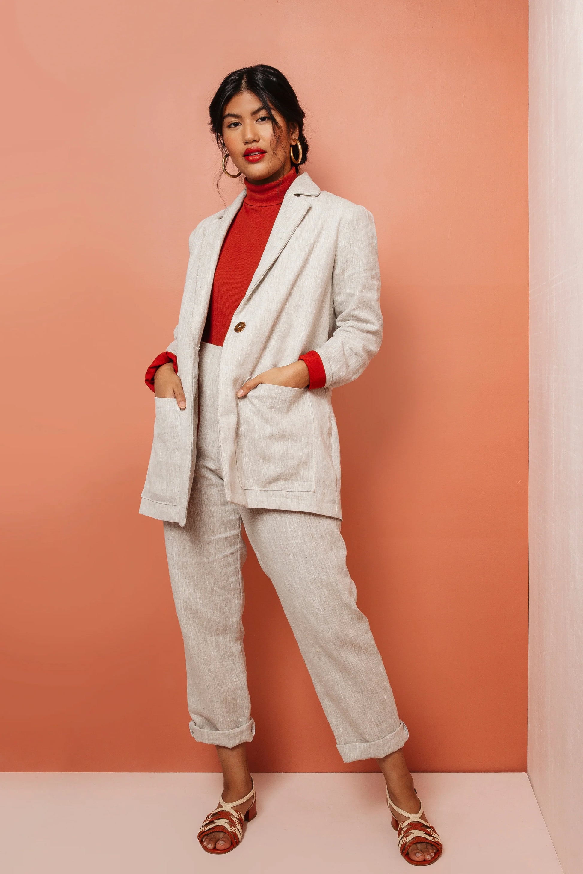 Woman wearing a light gray suit with red accents against a peach background
