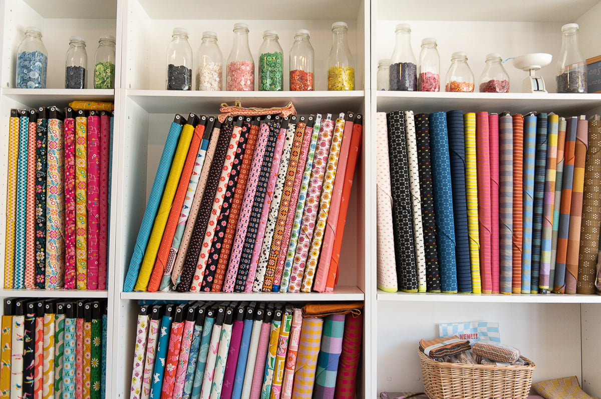 Shelves filled with colorful fabric rolls and small bottles on a white wall.