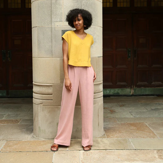 Woman in yellow top and pink pants standing against a stone wall.
