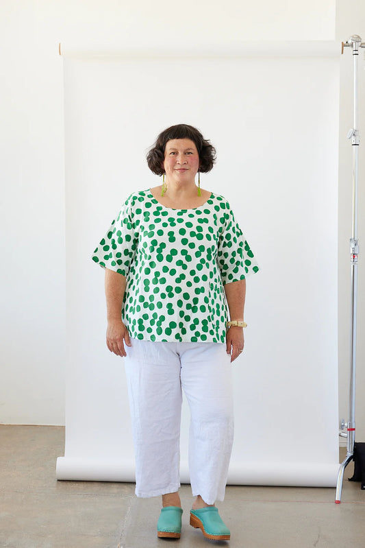 Woman wearing a white tunic with green dots in front of a white background 