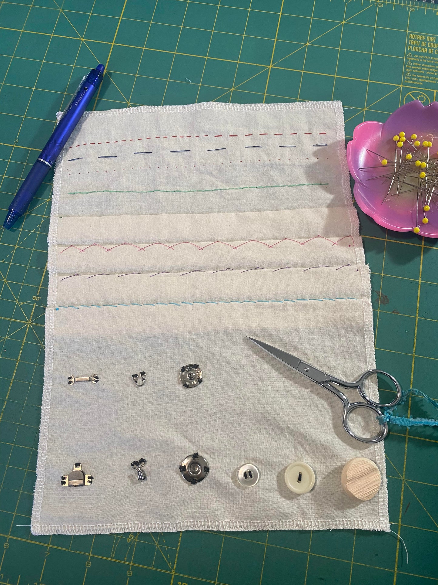 Displayed on a cutting mat is a sampler of hand stitching with scissors, pins and a marking pen.