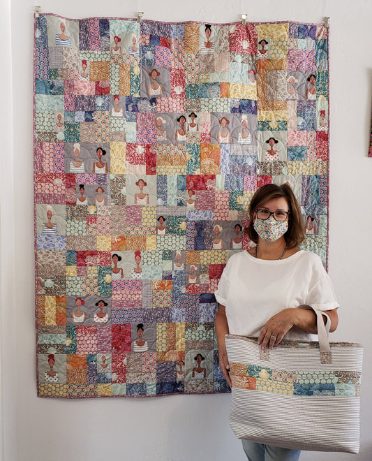 Julie stands in front of a patchwork quilt holding a coordinating bag