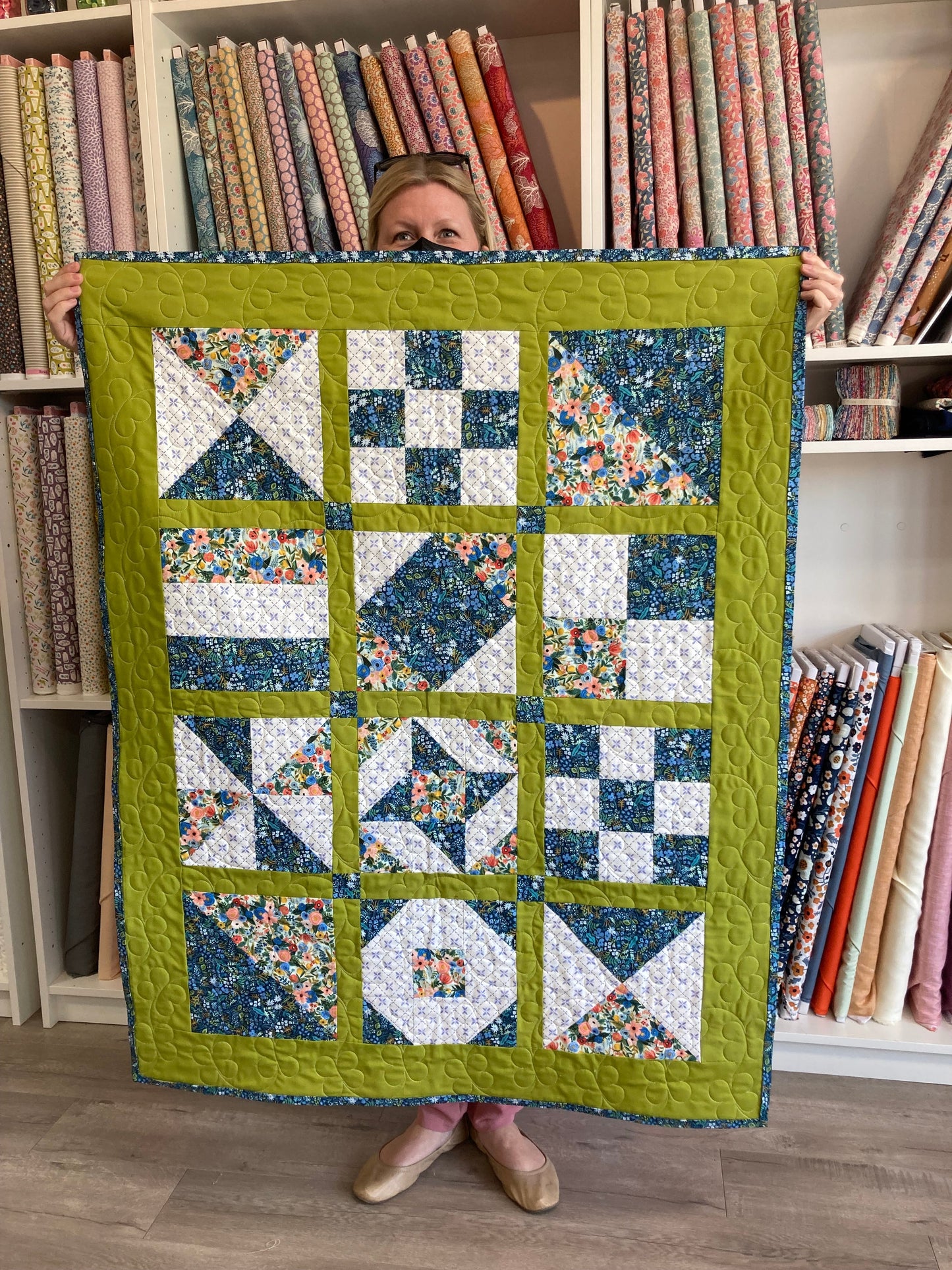 a blonde woman holds a quilt with a variety of blocks