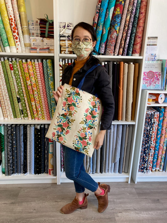 a person wearing a mask is displaying a tote bag